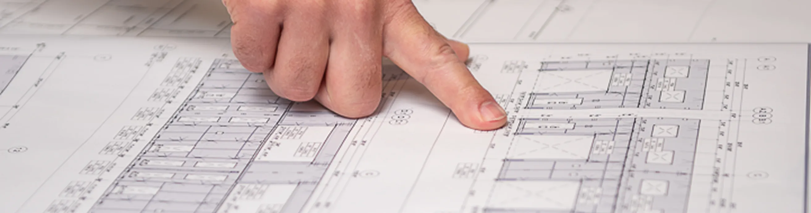 Close-up of a hand pointing at detailed architectural blueprints, highlighting a specific section of a technical drawing with measurements and structural details.