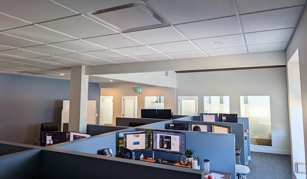 Modern office space with cubicles and computer workstations under a suspended ceiling.