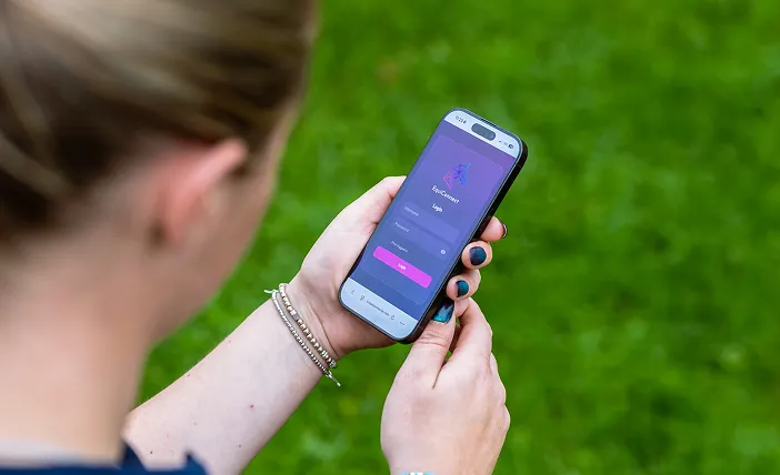 Person holding a smartphone showing a login screen with username and password fields against a green grass background.