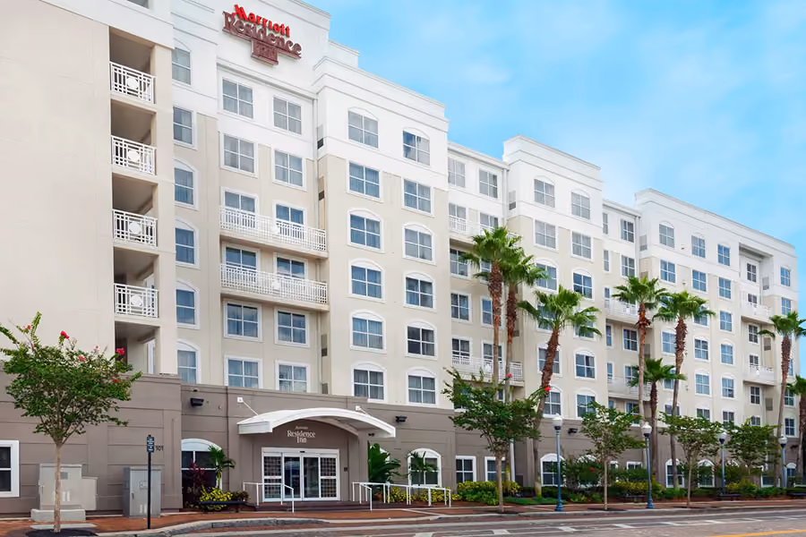 Front view of a multi-story Marriott Residence Inn hotel with palm trees and a clear blue sky.