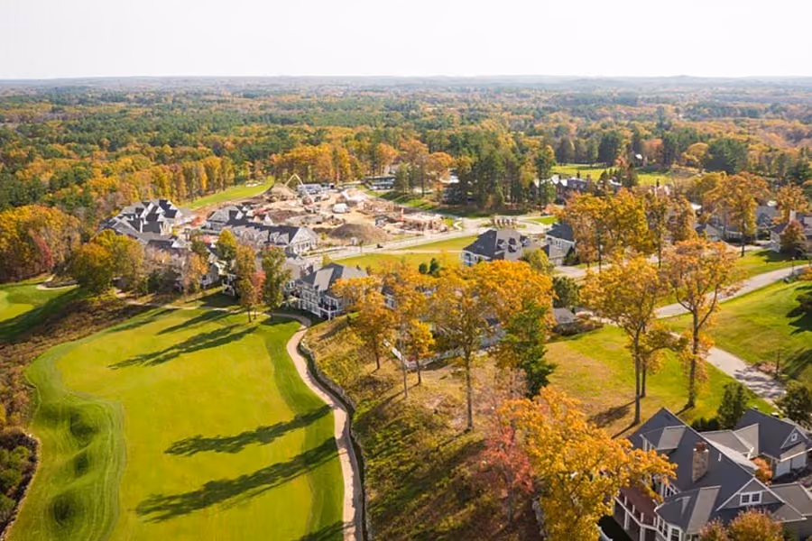 Aerial view of a residential neighborhood with houses, golf course, and trees during early autumn.