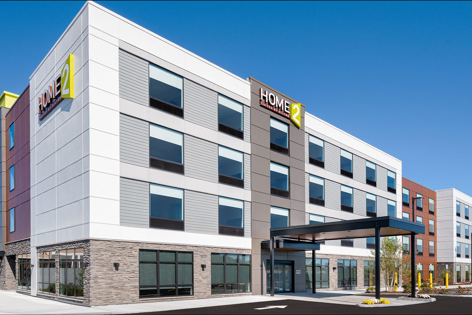 Four-story Home2 Suites by Hilton hotel with gray and white exterior, stone base, and covered front entrance.