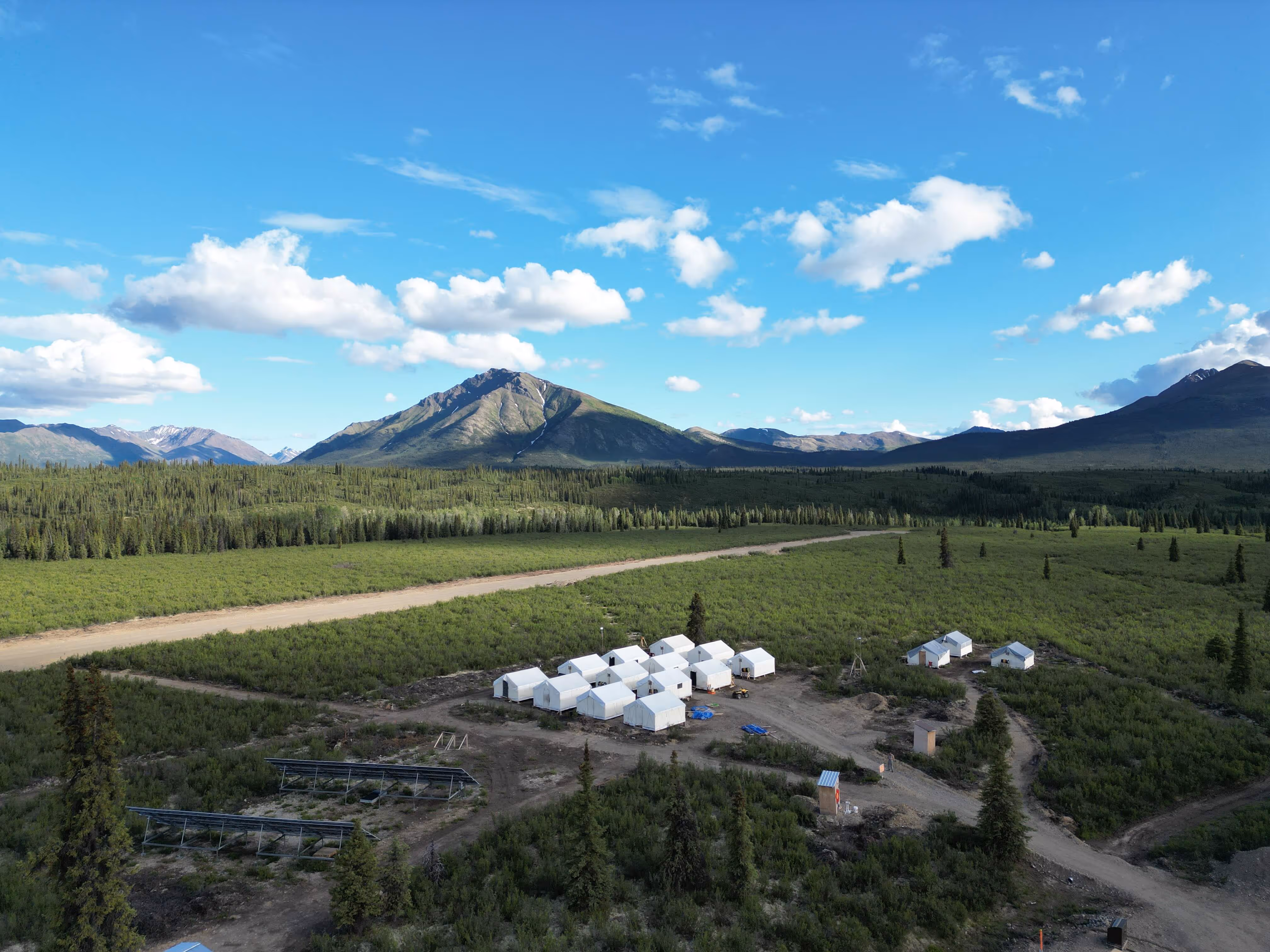 A large field with a mountain in the background and a few white cabins.