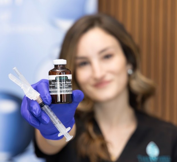 Smiling woman getting a vitamin injection in her upper arm from a gloved practitioner at ThrIVwell.