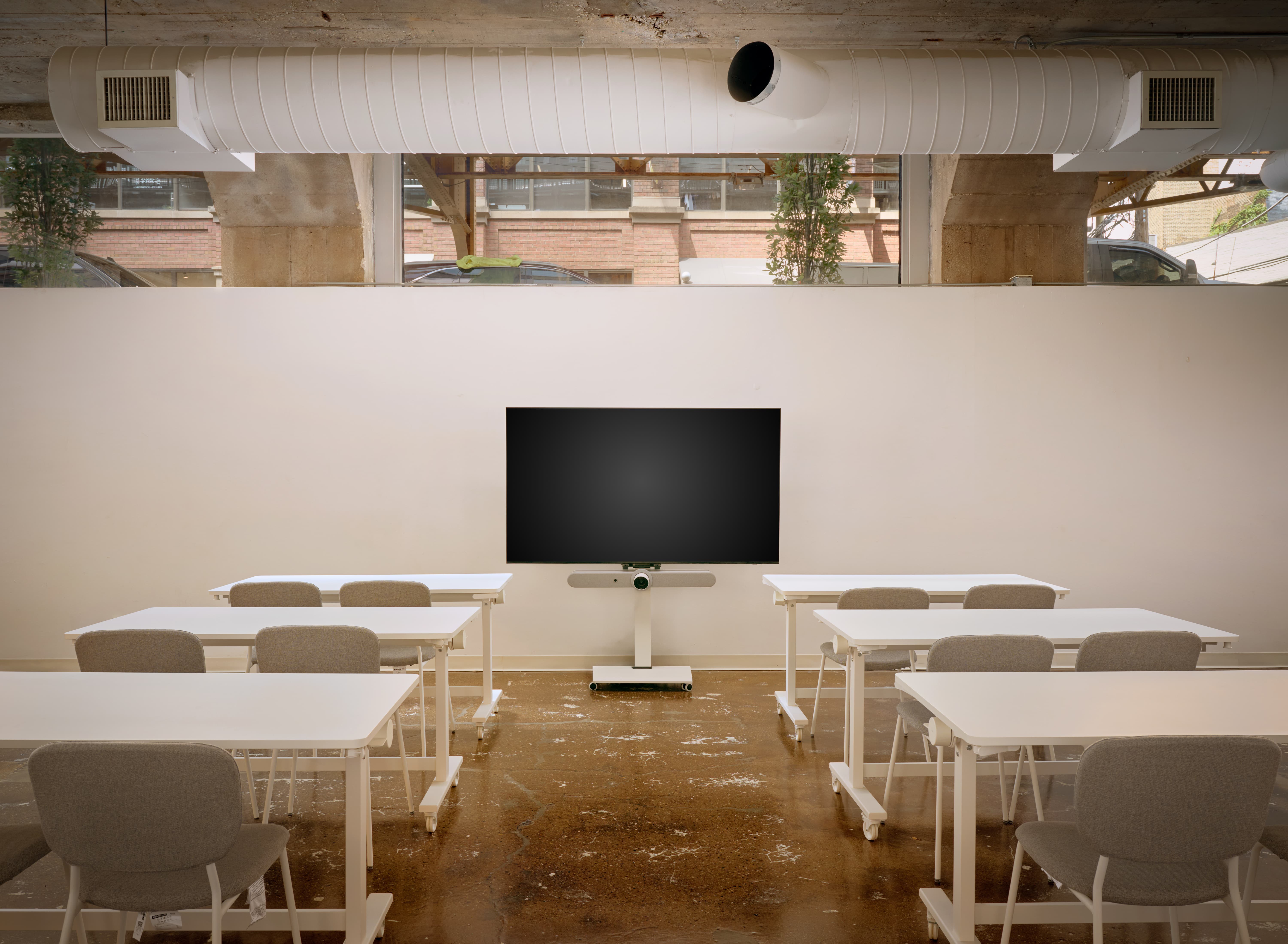 Meeting room at Two Thirty arranged classroom-style with white tables facing a wall-mounted display
