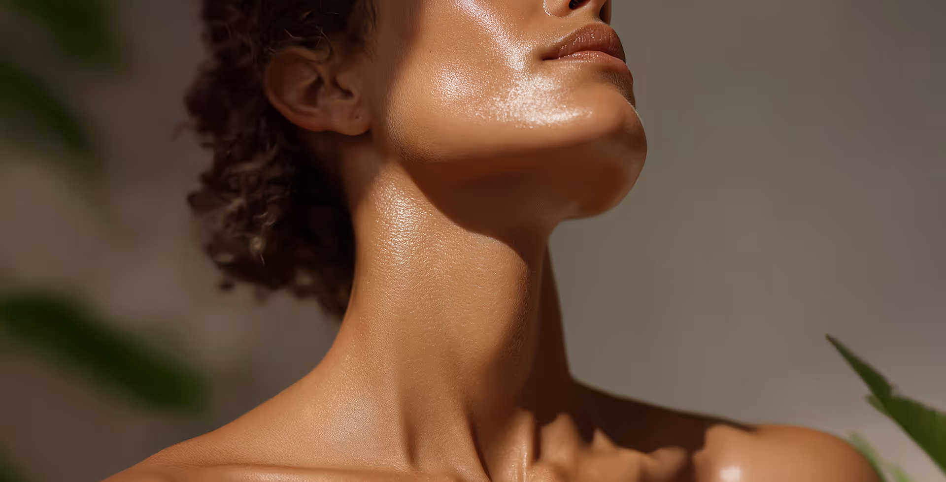Close-up of a woman’s glowing, moisturized neck and jawline with natural lighting and blurred green leaves in the background.
