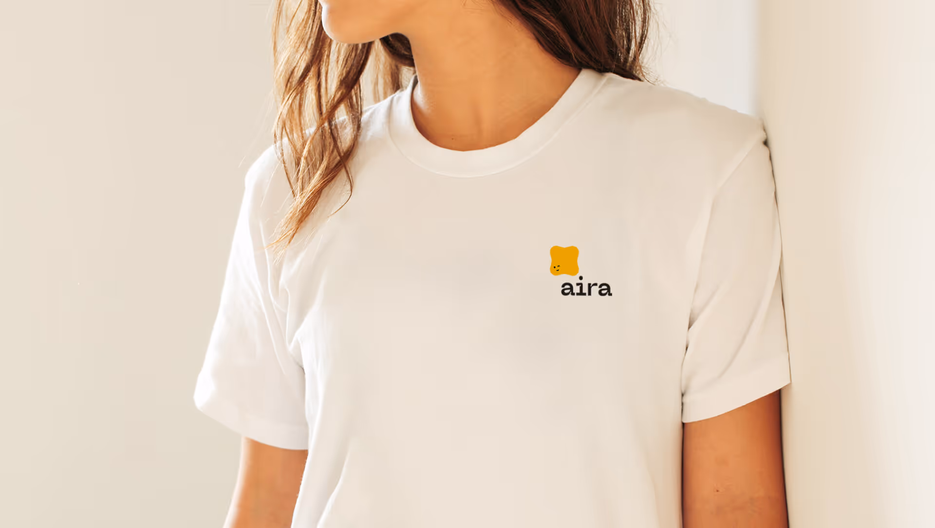 Woman wearing a white t-shirt with a small yellow bear graphic and the word 'aira' on the chest.