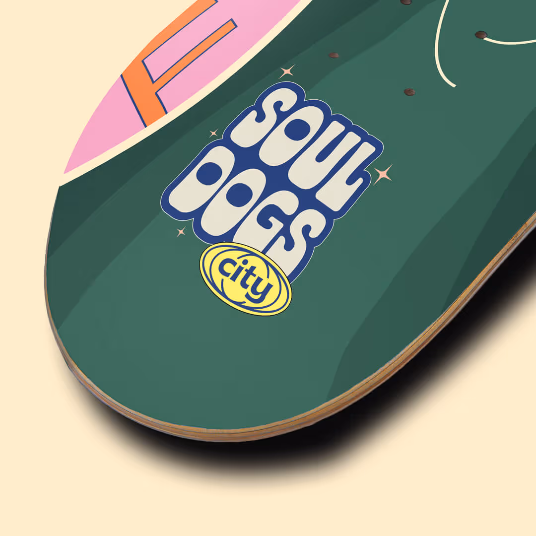 Close-up of a green skateboard deck with colorful retro text 'Soul Dogs city' printed on it.