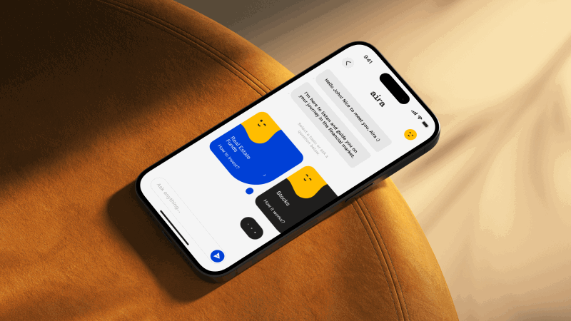 Smartphone on an orange fabric surface displaying a chat interface with Aira assistant, showing conversation bubbles about real estate and stocks.