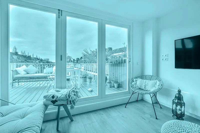 Private Wohnung mit einer Fensterfront. Im Hintergrund sieht man noch eine Terrasse mit Blumen.