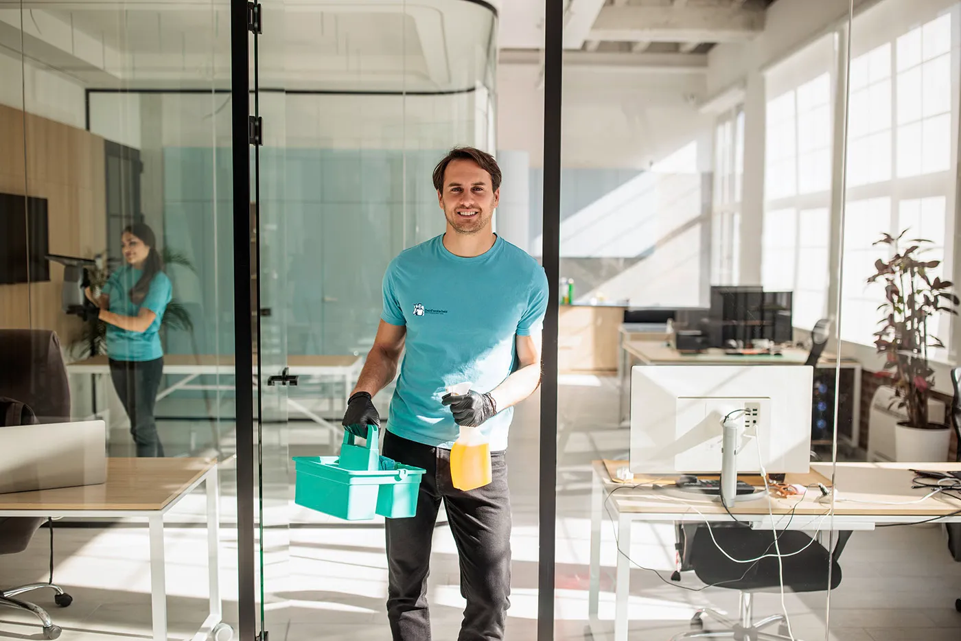 Ein junger Mann mit Reinigungsmaterialien in der Hand. Im Hintergrund sieht man ein Büro