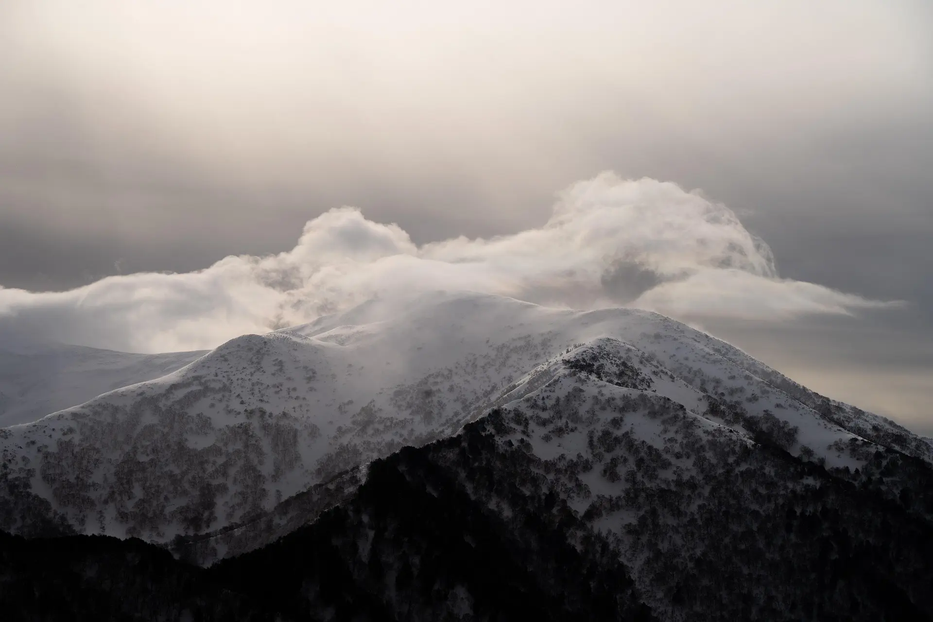 Snow-covered mountain peaks under a cloudy sky with mist and soft light.