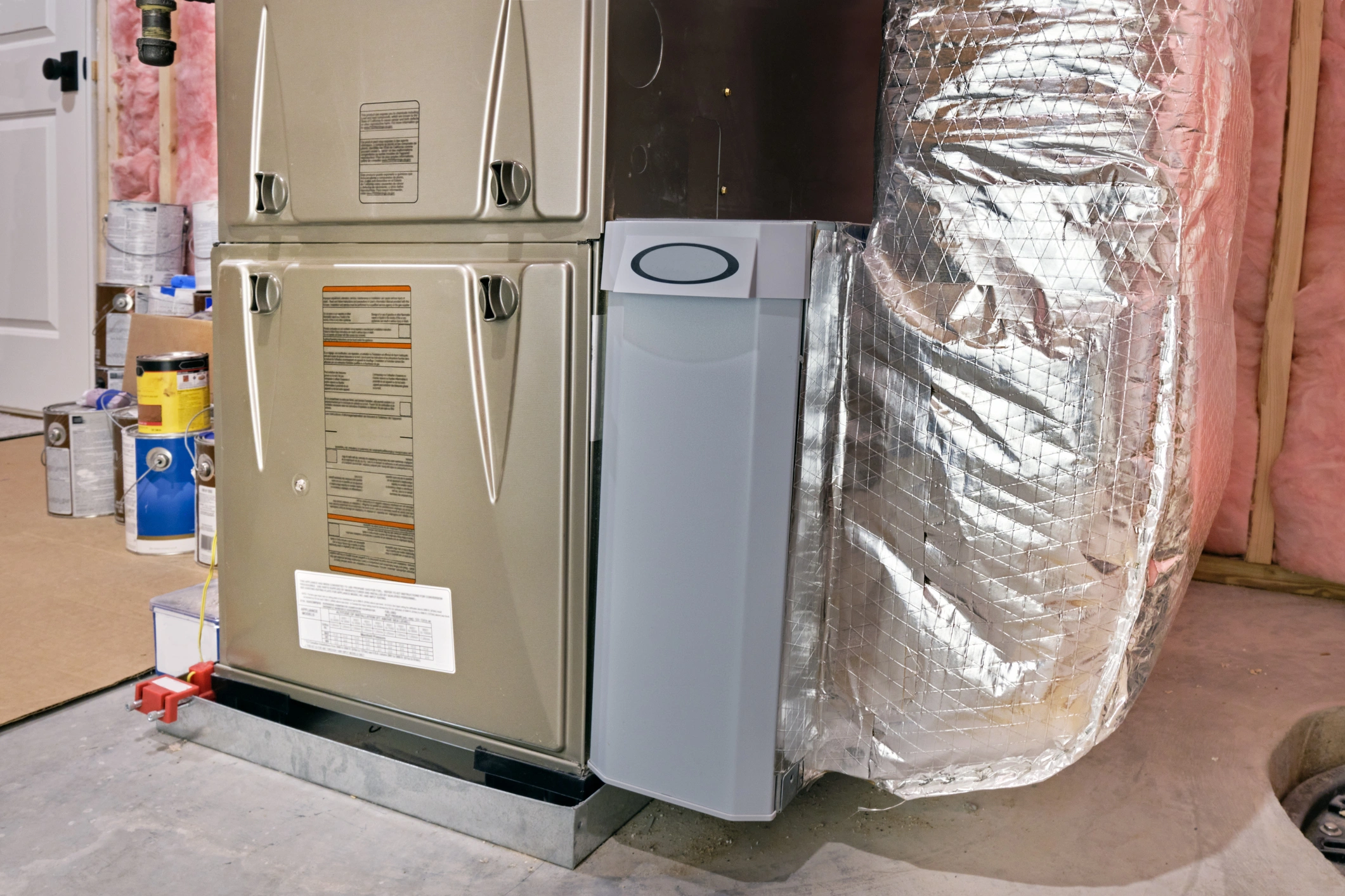 A modern furnace in a basement, surrounded by insulation and ductwork.