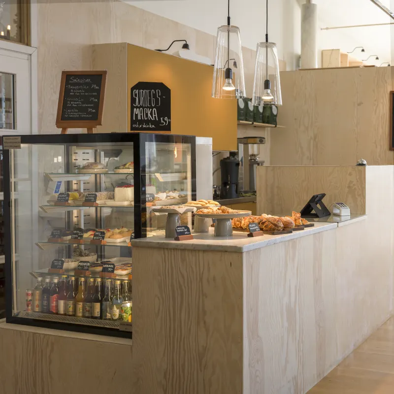 Ett kafé med diskar fyllda av bakverk och drycker i en ljus, modern inredning.