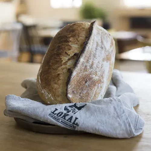 Ett rustikt bröd på en duk med texten 'LOKAL' på ett träbord i ett kafé.