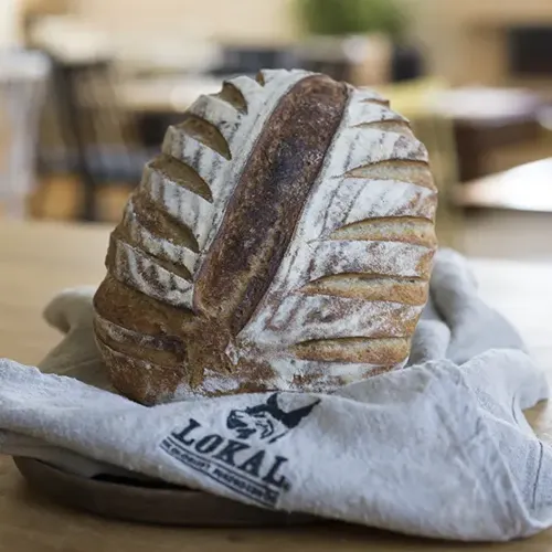 Hantverksbakat bröd med dekorativt snittad skorpa på en duk med Lokal Bageris logotyp.