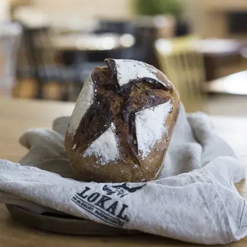 Limpa av hantverksbröd med stjärnformat mönster i skorpan, liggande på en duk märkt Lokal.