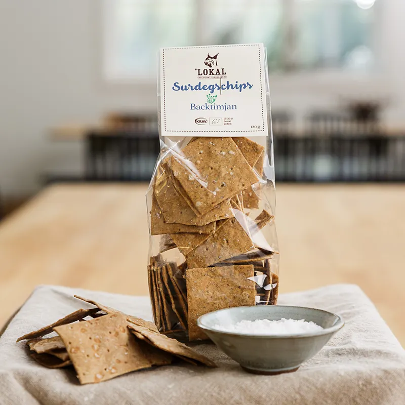 Påse med Lokals surdegschips med backtimjan, med en skål salt på en duk.