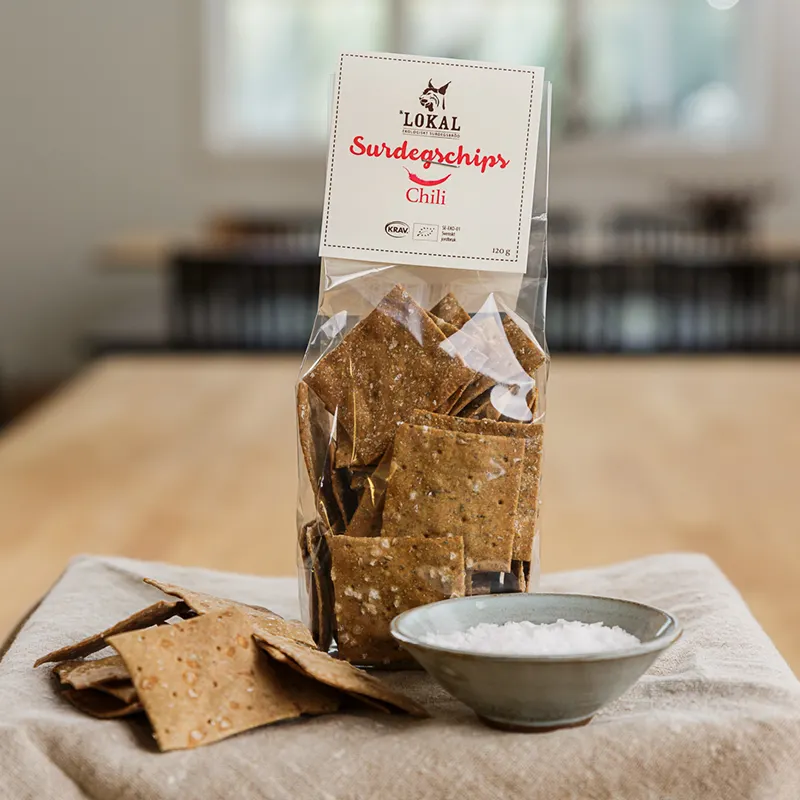 Förpackning med Lokals surdegschips med chilismak, med några bitar och en skål salt.