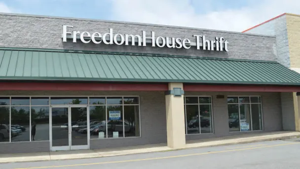Exterior of Freedom House Thrift store featuring a green awning and large windows, set against a cloudy sky.