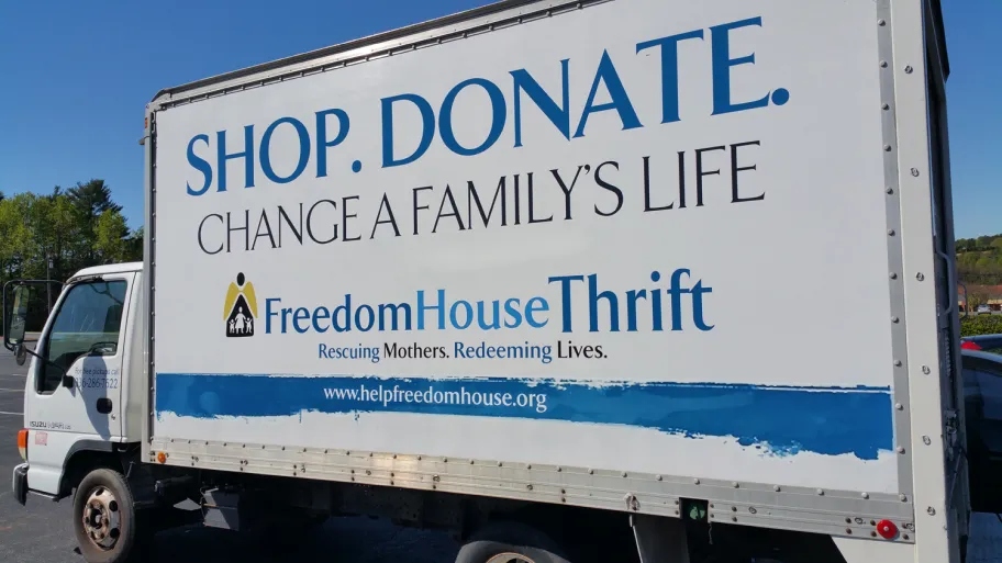 Side of a delivery truck advertising FreedomHouse Thrift: "Shop. Donate. Change a family's life. Rescuing Mothers. Redeeming Lives."