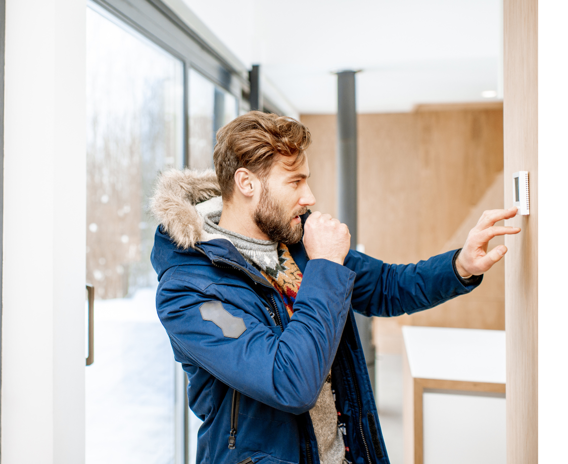 Man in winter clothing adjusting thermostat indoors, demonstrating energy efficiency in home heating during winter.