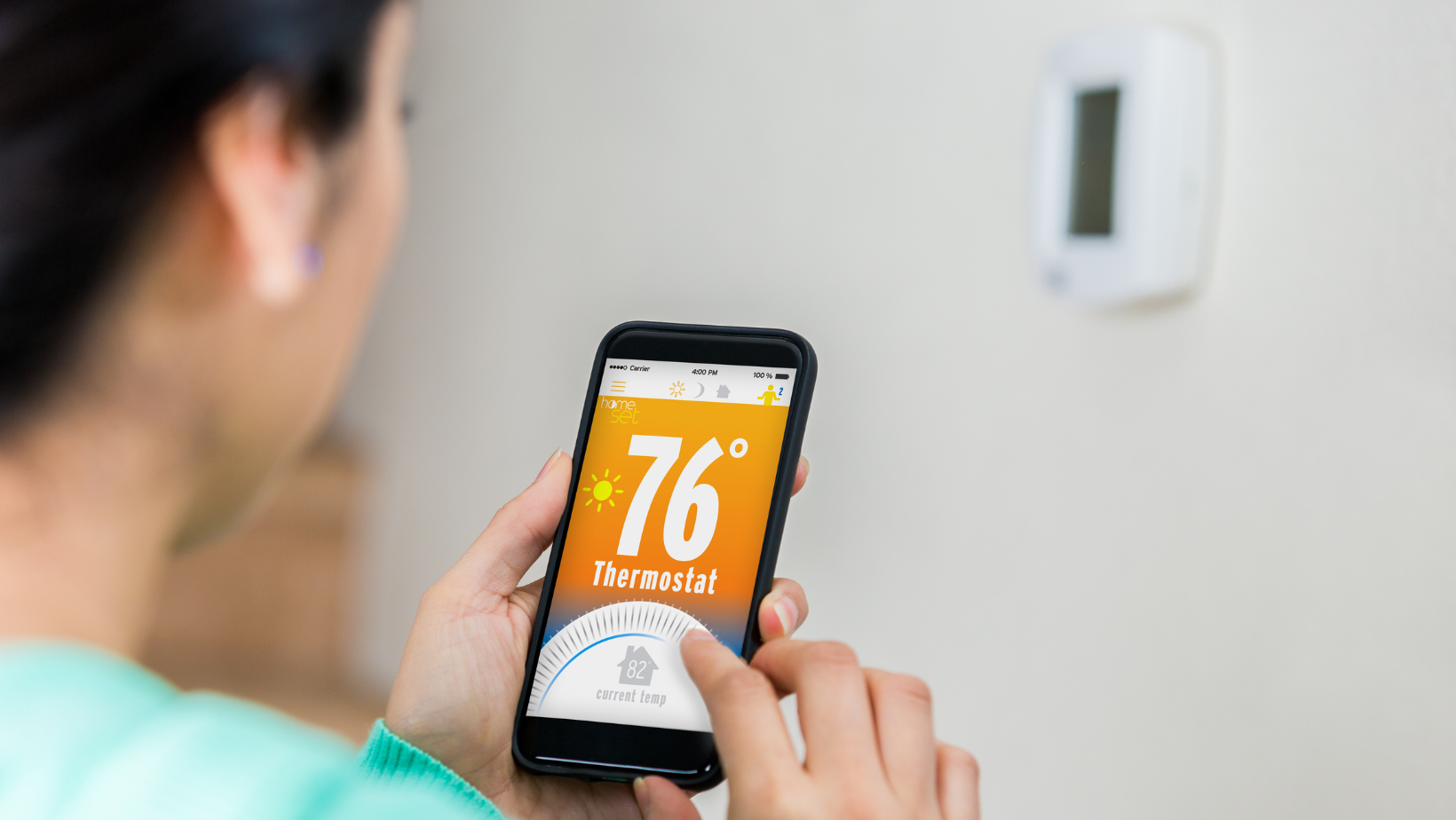 Person using smartphone to adjust thermostat settings, displaying current temperature of 76°F and home temperature of 82°F.