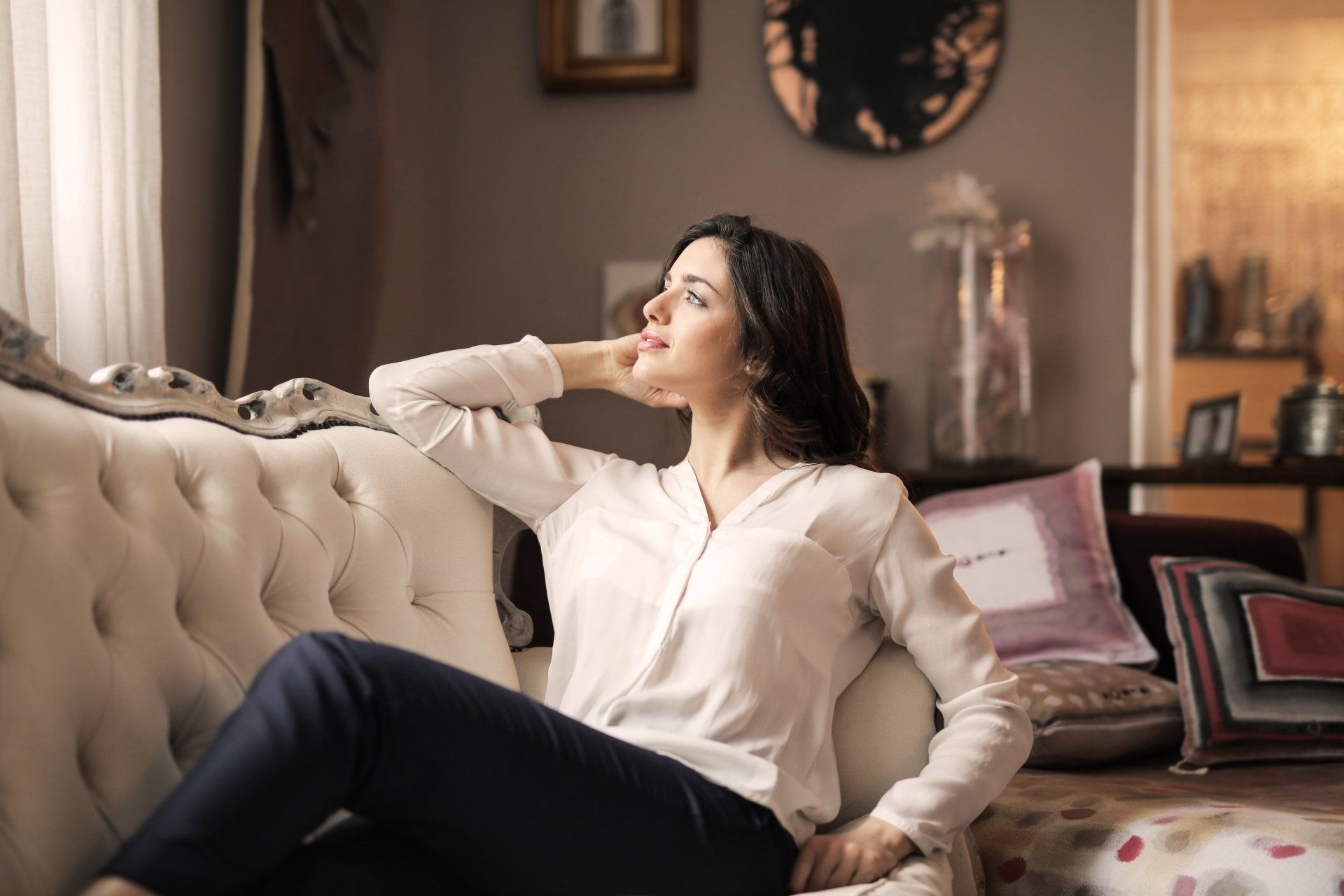 Woman relaxing on a tufted sofa, contemplating comfortably in a cozy indoor setting, emphasizing a serene atmosphere ideal for energy-efficient cooling solutions.