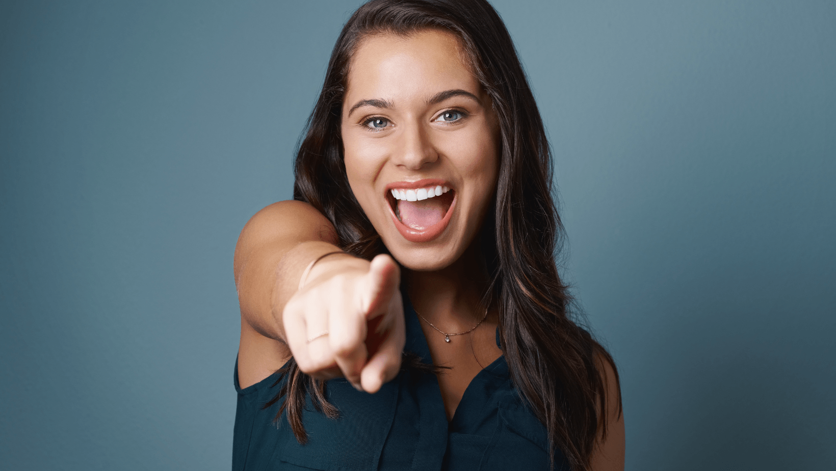 Smiling woman pointing at the camera, conveying enthusiasm and engagement, set against a blue background, relevant to HVAC service inquiries.