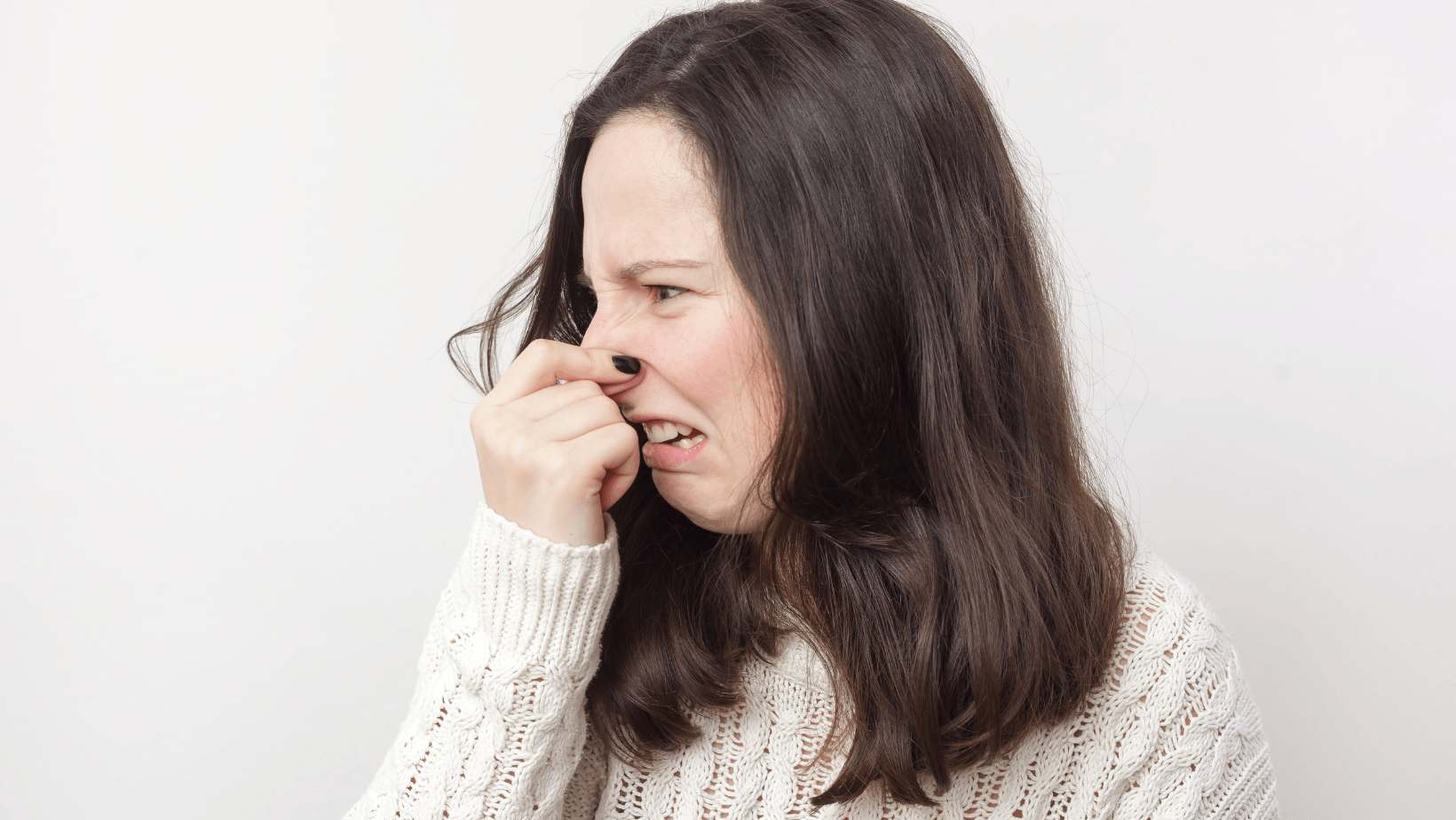 Woman grimacing while pinching her nose, expressing disgust, relevant to HVAC odors and maintenance issues.