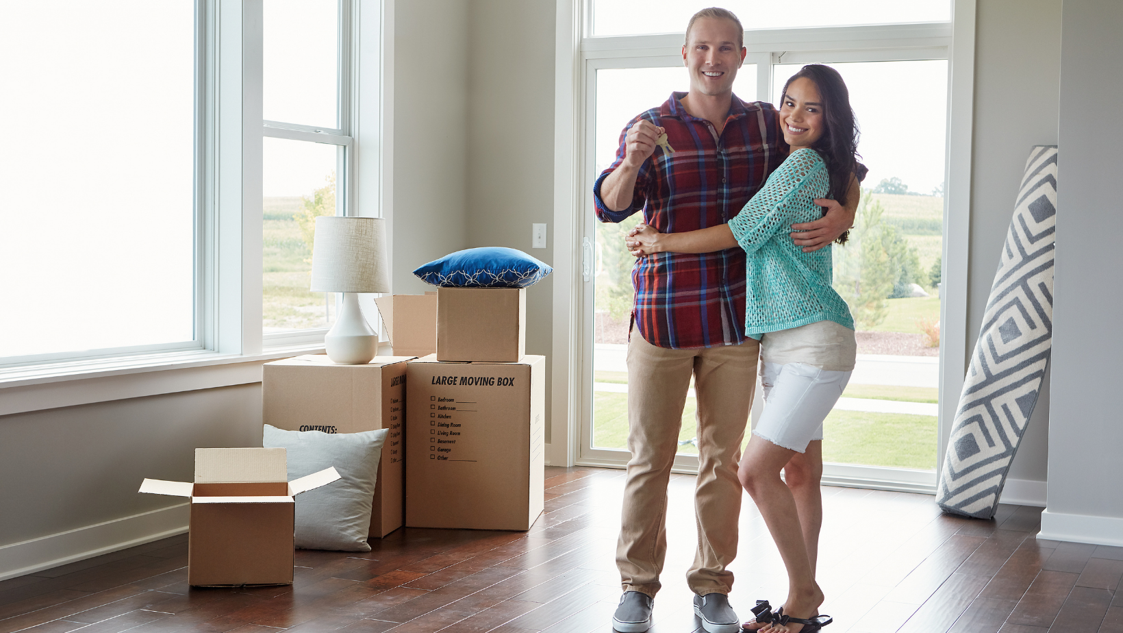 New homeowners celebrating in a bright living room surrounded by moving boxes, emphasizing the excitement of settling into a new space.