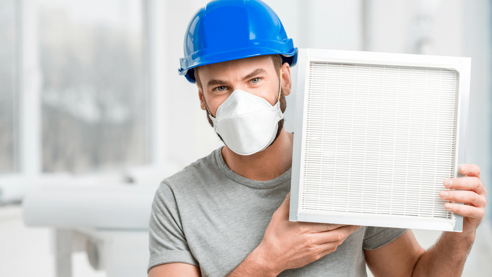 Man wearing a blue hard hat and face mask holding an air filter, emphasizing the importance of air quality and HVAC services.