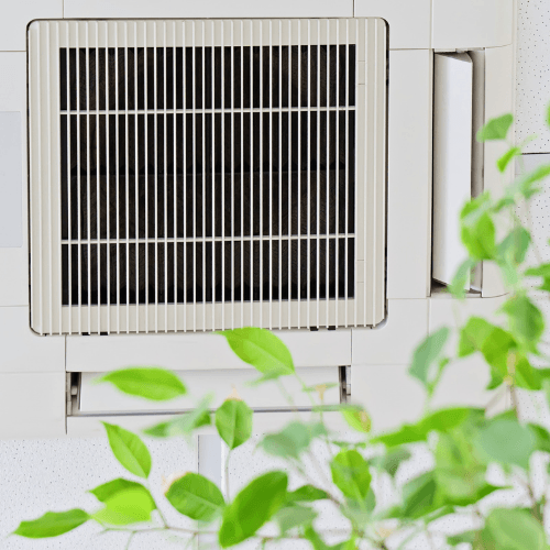 Ductless mini split air conditioning unit installed indoors, surrounded by green foliage, illustrating HVAC solutions for warmer weather and the importance of maintenance.