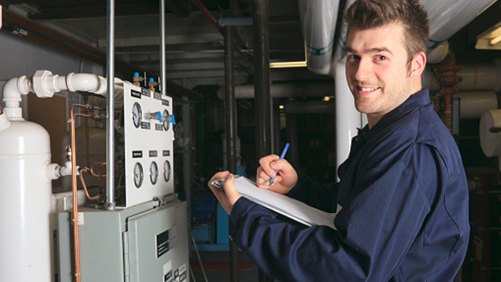 HVAC technician inspecting furnace equipment and taking notes in a maintenance setting.