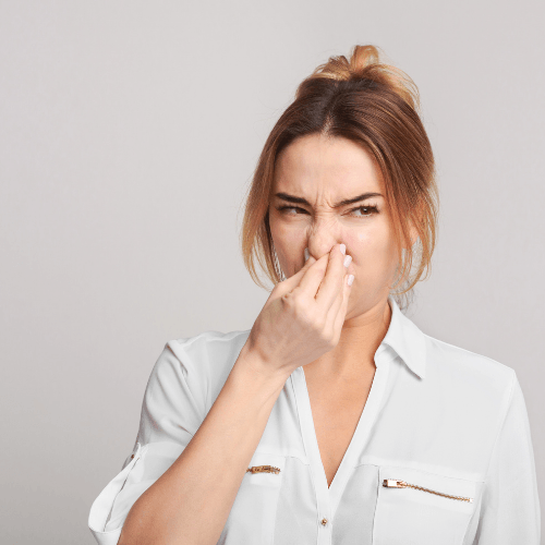 Woman pinching her nose in disgust, indicating unpleasant odor, relevant to HVAC odor issues and maintenance guidance.