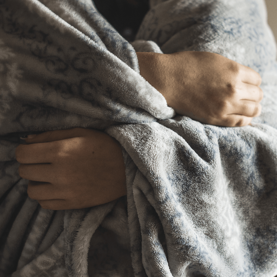Person wrapped in a cozy gray blanket, emphasizing warmth and comfort during winter, relevant to HVAC tips for efficient heating and reducing energy costs.