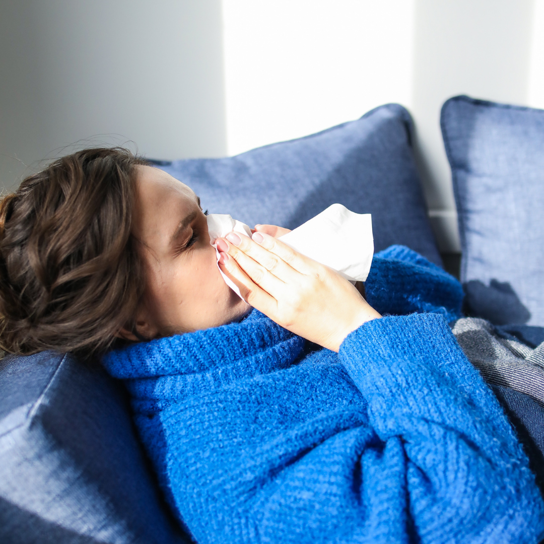 Woman in blue sweater using a tissue while resting on a couch, illustrating symptoms of respiratory issues related to poor indoor air quality.