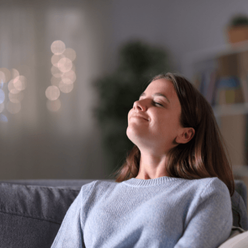 Woman enjoying fresh indoor air while relaxing on a couch, representing improved air quality from HVAC services and air filter replacement.