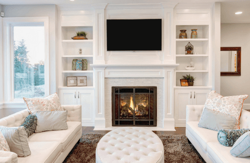 Cozy living room featuring white sofas, a circular tufted ottoman, a modern fireplace, and built-in shelves, emphasizing indoor comfort and HVAC efficiency.