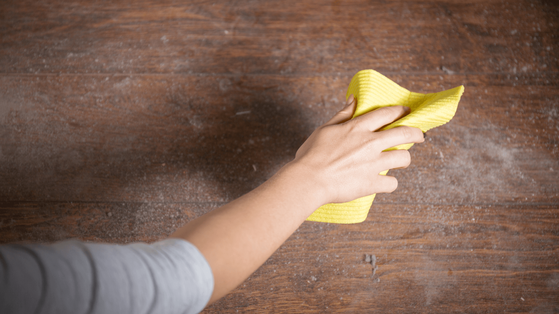 Person using a yellow cloth to wipe dust off a wooden surface, emphasizing home cleaning and indoor air quality improvement.