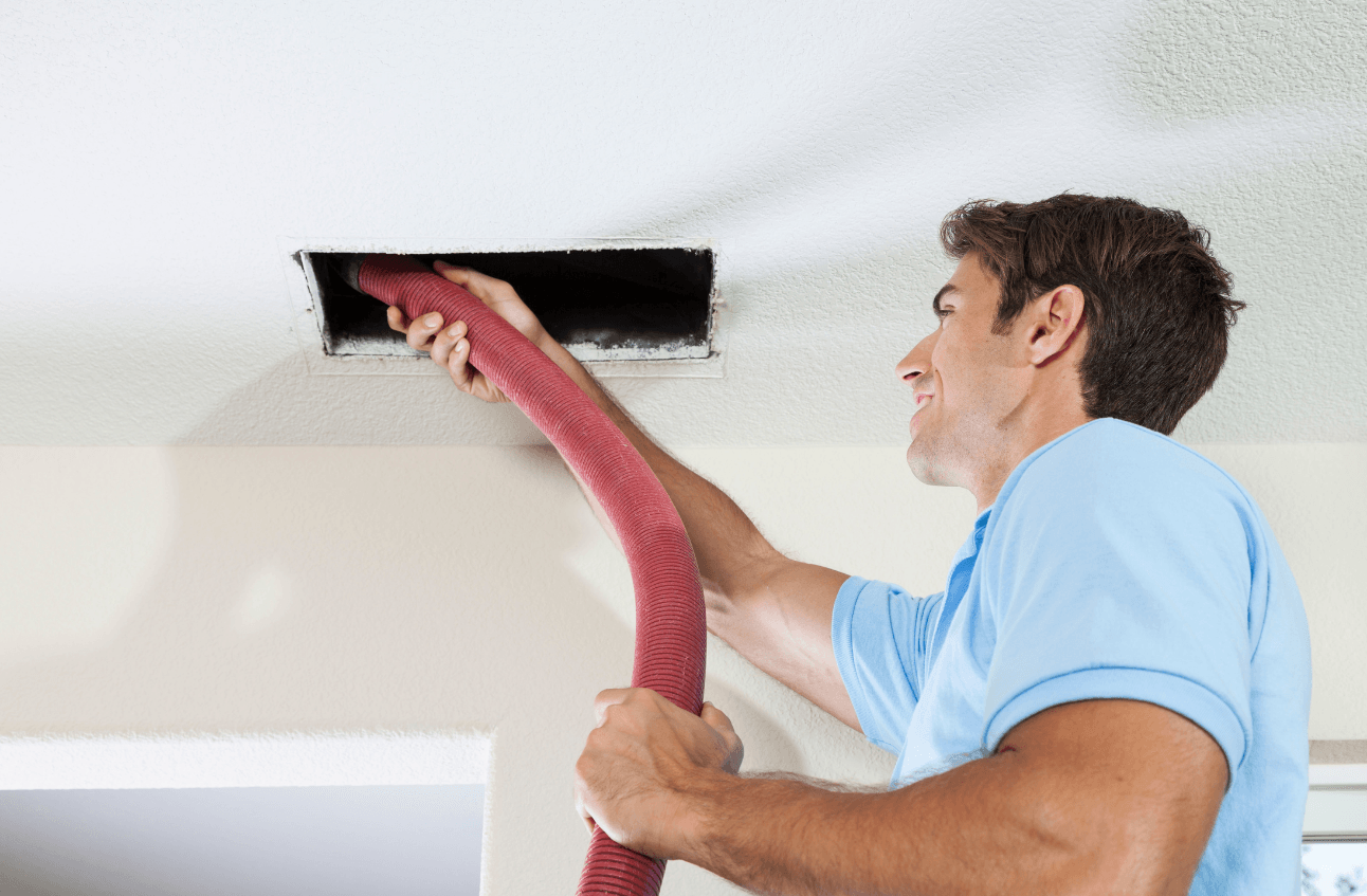 Technician using a vacuum hose to clean air ducts, promoting improved indoor air quality and HVAC maintenance.