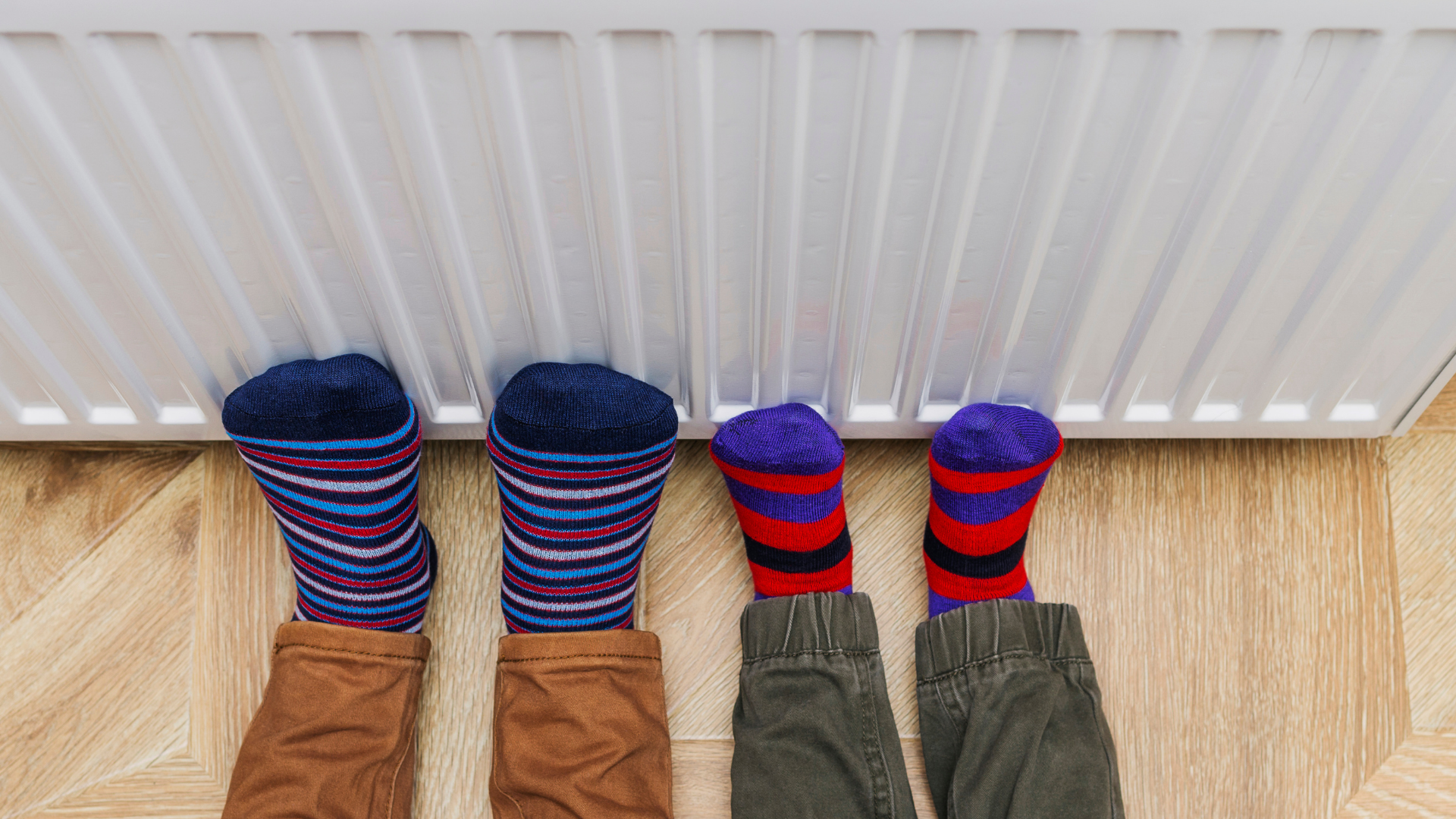 Children's feet in colorful socks warming by a radiator, illustrating the importance of heater functionality during winter.