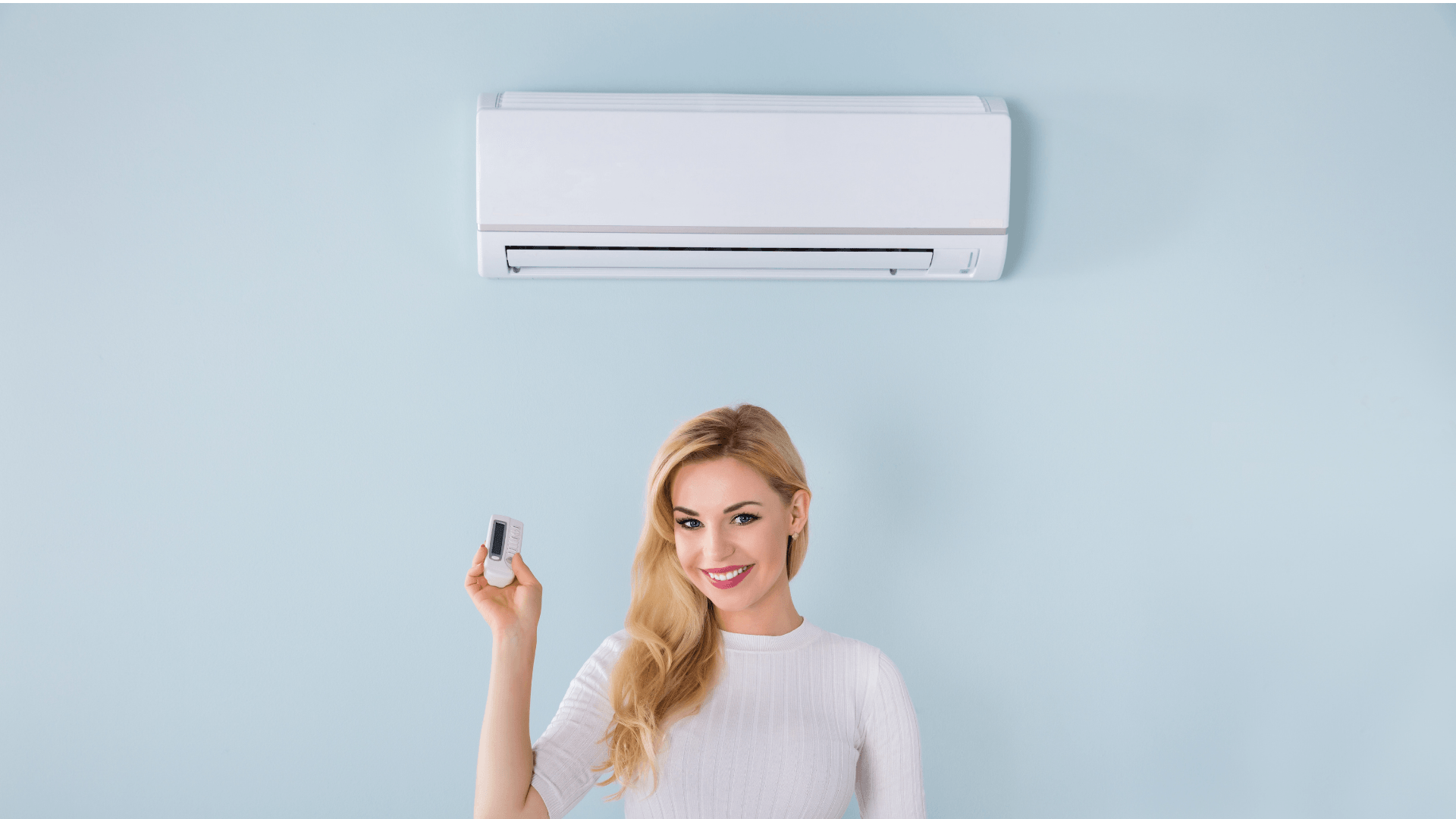 Woman holding remote control for ductless mini-split air conditioning unit mounted on light blue wall, illustrating HVAC system maintenance and temperature regulation.