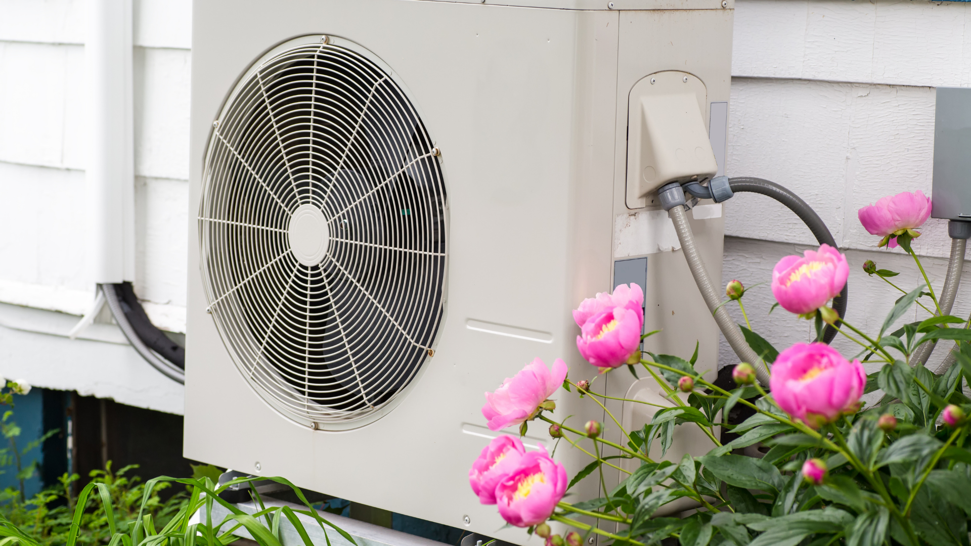 Ductless mini split air conditioning unit installed outside a home, surrounded by pink peony flowers, illustrating HVAC systems and maintenance importance.