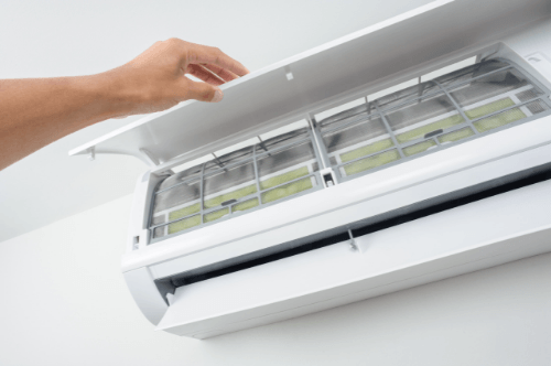 Hand opening the cover of an HVAC unit to access and clean the air filters for improved indoor air quality and system efficiency.