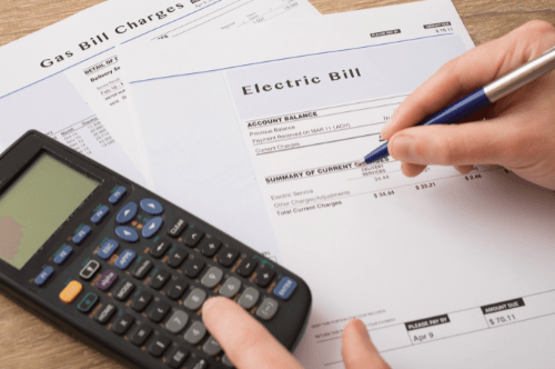 Person reviewing electric bill and gas bill statements with calculator and pen, illustrating the importance of monitoring utility costs related to HVAC efficiency.