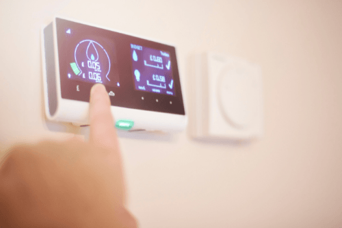 Smart thermostat being adjusted, displaying energy usage metrics and settings, illustrating remote access and smart-learning features for HVAC efficiency.