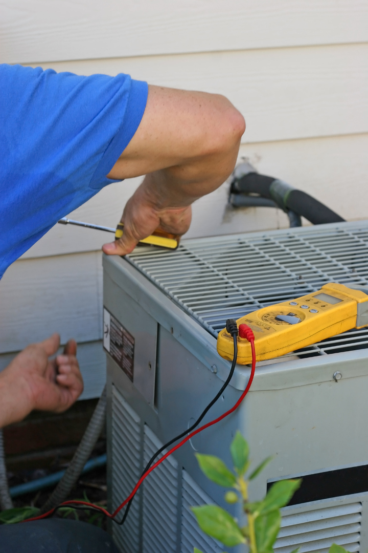Technician repairing air conditioner unit with screwdriver and multimeter, emphasizing HVAC maintenance services for optimal performance.