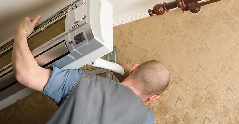 A technician is using a screwdriver to open up and repair a ductless mini-split indoor unit