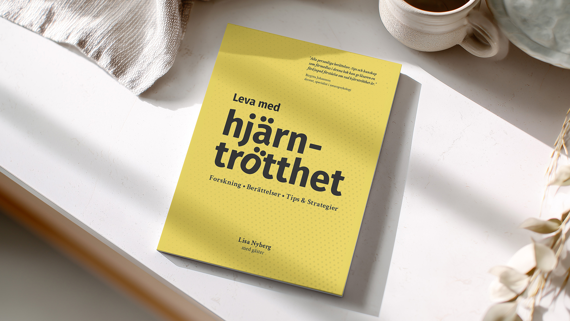 Leva med hjarntrotthet-book lying in sunlight on white desk with a cup of coffee.